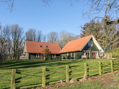Two green houses with red roofs on a grassy hill behind a wooden fence at Lime Tree Lodge Swarland near Alnwick
