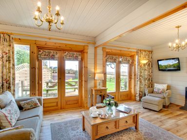 A living room with wooden framed glass doors sofa armchair coffee table with tea set and flowers at Lime Tree Lodge Swarland near Alnwick