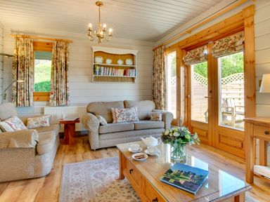 A living room with sofas a coffee table with tea set and flowers and wooden doors at Lime Tree Lodge Swarland near Alnwick