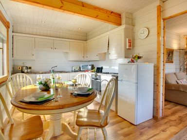 A kitchen with a wooden dining table set for four with wine glasses and white cabinets at Lime Tree Lodge in Swarland near Alnwick