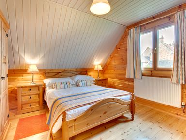 A bedroom with a wooden bed and nightstands with lamps at Lime Tree Lodge in Swarland near Alnwick