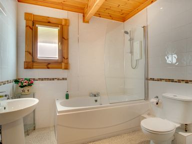 A bathroom with a bathtub shower toilet sink and a window with wooden frame at Lime Tree Lodge in Swarland near Alnwick