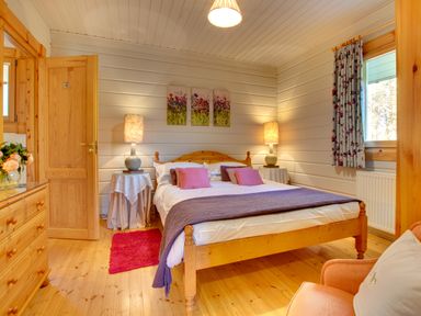 A bedroom with a wooden bed and side tables with lamps a wooden dresser and an armchair at Lime Tree Lodge Swarland near Alnwick