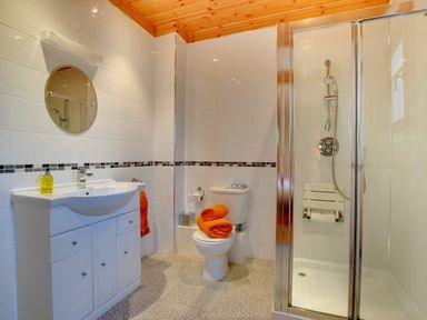 A bathroom with a white sink cabinet a round mirror a toilet with orange towels and a glass shower enclosure at Lime Tree Lodge in Swarland near Alnwick