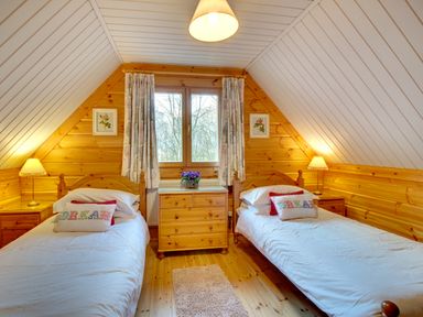 A bedroom with two single beds bedside tables lamps and a chest of drawers under a window at Lime Tree Lodge Swarland near Alnwick