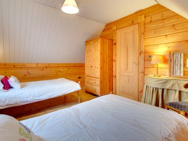 A bedroom with two beds a wooden wardrobe a door and a lamp on a table at Lime Tree Lodge Swarland near Alnwick