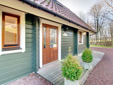 The entrance of a green wooden house with a brown door two windows and two potted plants on a wooden porch at Lime Tree Lodge Swarland near Alnwick