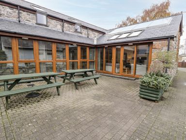 An outdoor patio area with two green picnic tables and wooden framed glass doors at Ddol Helyg Barn in Llanrug