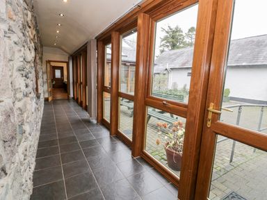 A hallway with stone wall on one side and large wooden framed windows on the other side at Ddol Helyg Barn in Llanrug