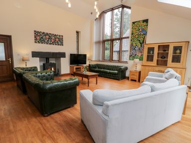 A living room with leather sofas a wooden coffee table TV and large windows at Ddol Helyg Barn in Llanrug