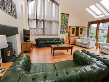 A living room with green leather sofas wood furniture and a fireplace at Ddol Helyg Barn in Llanrug