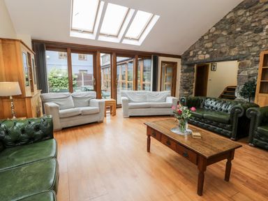 A living room with green and white sofas a wooden coffee table and a stone wall at Ddol Helyg Barn in Llanrug