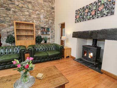 A living room with green leather sofas a wooden coffee table with flowers a stone wall and a fireplace at Ddol Helyg Barn in Llanrug