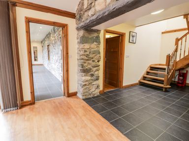 A hallway with tiled and wooden floors stone walls wooden doors and a staircase at Ddol Helyg Barn in Llanrug