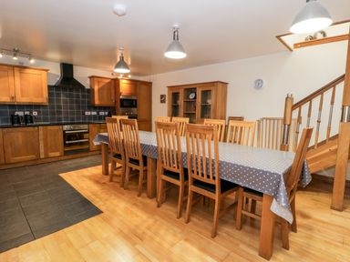 A kitchen and dining area with wooden cabinets and a long dining table with chairs at Ddol Helyg Barn in Llanrug