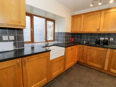 A kitchen with wooden cabinets black countertops a white sink two black kettles and a toaster at Ddol Helyg Barn in Llanrug