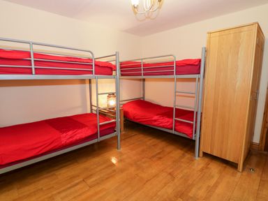 A bedroom with two metal bunk beds with red bedding a wooden wardrobe and a small bedside table with a lamp at Ddol Helyg Barn in Llanrug
