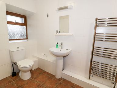 A bathroom with a toilet, sink, mirror, towel radiator, and frosted window at Ddol Helyg Barn in Llanrug