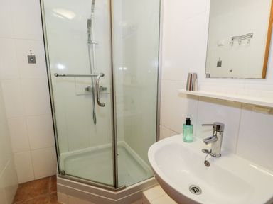 A bathroom with a glass shower enclosure a white sink with a faucet and soap dispenser at Ddol Helyg Barn in Llanrug