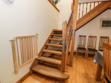 A wooden staircase next to a baby gate and wooden chairs along a wall near a dining table at Ddol Helyg Barn in Llanrug