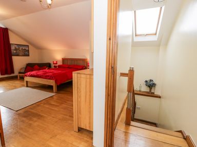 A bedroom with a red bedspread next to a staircase with a skylight window at Ddol Helyg Barn in Llanrug
