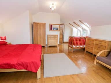 A bedroom with wooden bed and red bedding a wardrobe a dresser a crib and windows with skylights at Ddol Helyg Barn in Llanrug
