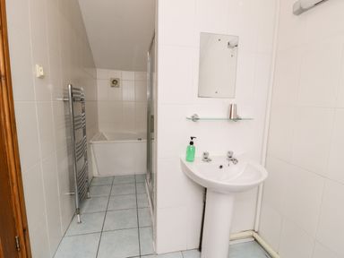 A bathroom with a pedestal sink mirror glass shelf soap dispenser heated towel rail bathtub and tiled walls and floor at Ddol Helyg Barn in Llanrug