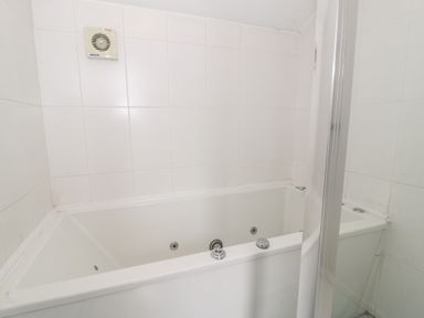 A white corner bathtub with jets and white tiled walls in a bathroom at Ddol Helyg Barn in Llanrug
