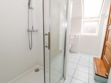 A bathroom with a glass shower enclosure a toilet a window a wooden door and a wooden bench at Ddol Helyg Barn in Llanrug