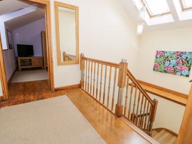 A hallway with a staircase wooden floor a mirror and a doorway leading to a room with a TV at Ddol Helyg Barn in Llanrug