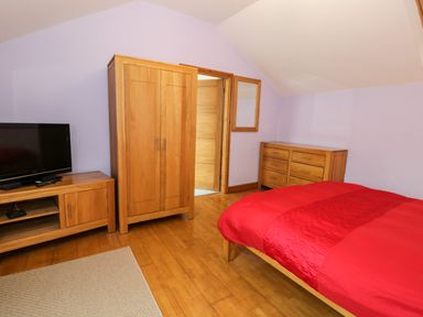 A bedroom with wooden furniture a television bed with red bedding and a wooden dresser at Ddol Helyg Barn in Llanrug
