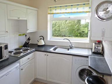 A kitchen with white cabinets a stove microwave kettle toaster and washing machine under a window at Seascope in Kessingland near Lowestoft
