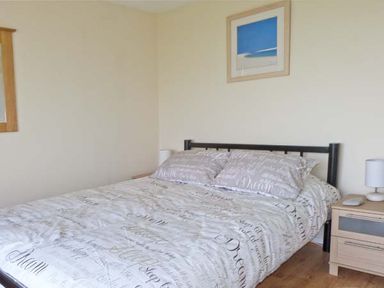 A bedroom with a bed with printed bedding a nightstand with a lamp and a framed picture on the wall at Seascope in Kessingland near Lowestoft