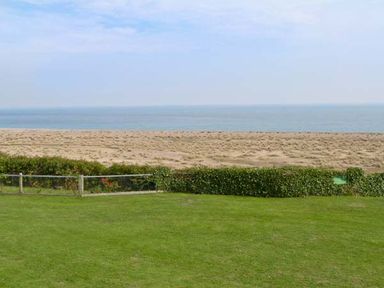 A grassy lawn with a hedge and fence overlooking a sandy beach and the sea at Seascope in Kessingland near Lowestoft