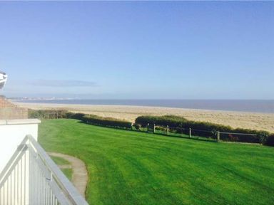 A grassy lawn with a pathway and a view of a sandy beach and the sea at Seascope in Kessingland near Lowestoft