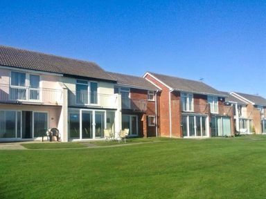 A row of two story houses with balconies and patios overlooking a grassy lawn at Seascope in Kessingland near Lowestoft