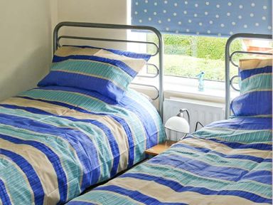 A bedroom with two single beds with striped bedding and a window with a blue polka dot blind at Seascope in Kessingland near Lowestoft