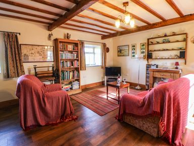 A living room with two armchairs covered with red throws a wooden bookshelf a small coffee table and a television at Cherry Tree Cottage Soulby near Kirkby Stephen