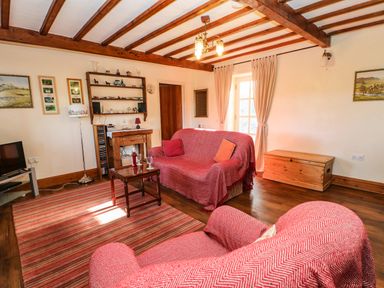 A living room with two covered sofas a wooden coffee table a TV stand with television and a rug at Cherry Tree Cottage in Soulby near Kirkby Stephen