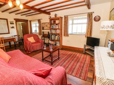 A living room with red covered sofa and armchair wooden bookshelf and striped rug at Cherry Tree Cottage Soulby near Kirkby Stephen