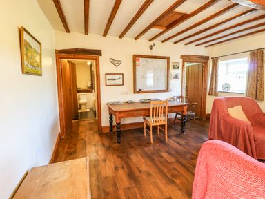 A room with a wooden table and chairs a red covered armchair and a view into a bathroom at Cherry Tree Cottage Soulby near Kirkby Stephen