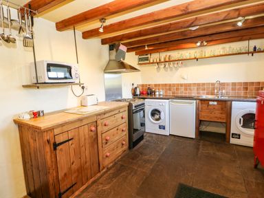 A kitchen with wooden cabinets a microwave oven washing machine and kitchen utensils at Cherry Tree Cottage Soulby near Kirkby Stephen