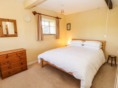 A bedroom with a double bed a wooden dresser a small window with curtains and a small side table at Cherry Tree Cottage in Soulby near Kirkby Stephen