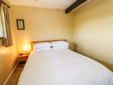 A bedroom with a double bed white bedding wooden headboard and a nightstand with a lamp at Cherry Tree Cottage Soulby near Kirkby Stephen