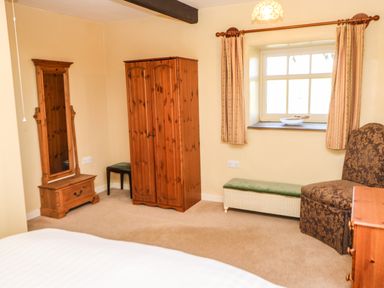 A bedroom with a wooden wardrobe mirror a chair and a window with curtains at Cherry Tree Cottage Soulby near Kirkby Stephen