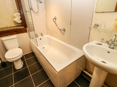 A bathroom with a toilet, bathtub with shower, and a sink at Cherry Tree Cottage in Soulby near Kirkby Stephen