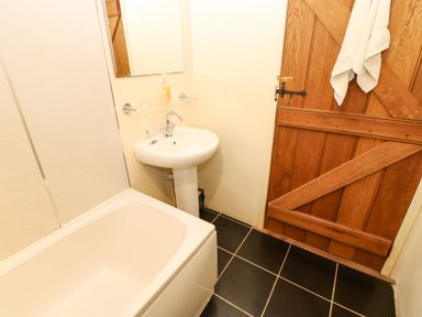 A bathroom with a bathtub a pedestal sink a mirror a wooden door and a towel hanging at Cherry Tree Cottage in Soulby near Kirkby Stephen