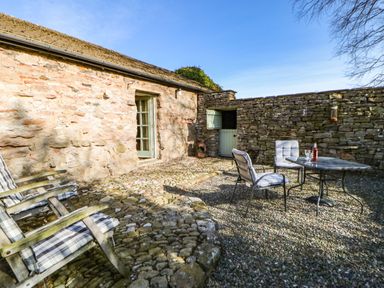 An outdoor stone patio with two cushioned wooden chairs and a metal table with two cushioned metal chairs at Cherry Tree Cottage in Soulby near Kirkby Stephen