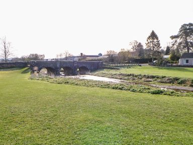 A stone bridge over a small river with grassy fields and trees surrounding it at Cherry Tree Cottage in Soulby near Kirkby Stephen