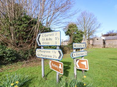 Road signs indicating directions to C Garrett Gt Asby Orton L Musgrave Gt Musgrave Appleby and K Stephen in a grassy area with trees and buildings nearby at Cherry Tree Cottage in Soulby near Kirkby Stephen
